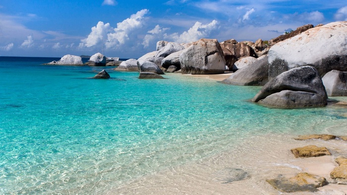 Crystal clear turquoise water and large granite boulders on a sandy beach.