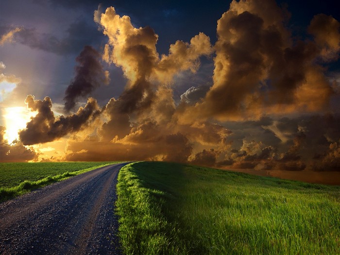 Dramatic sunset over a grassy hill with a winding road