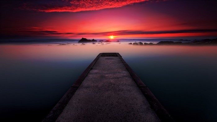 Concrete pier leading to ocean sunset with mist