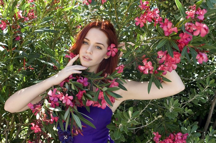 Redhead woman in purple dress surrounded by pink flowers