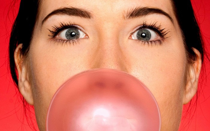 Close up of a woman blowing pink bubble gum