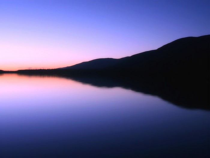 Silhouette of mountains reflected in a lake at dusk