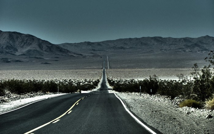 Desert highway stretching towards distant mountains under a dark sky