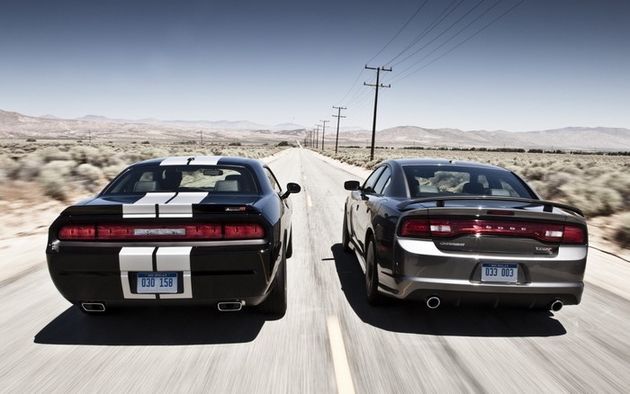 Two Dodge muscle cars driving on a desert highway