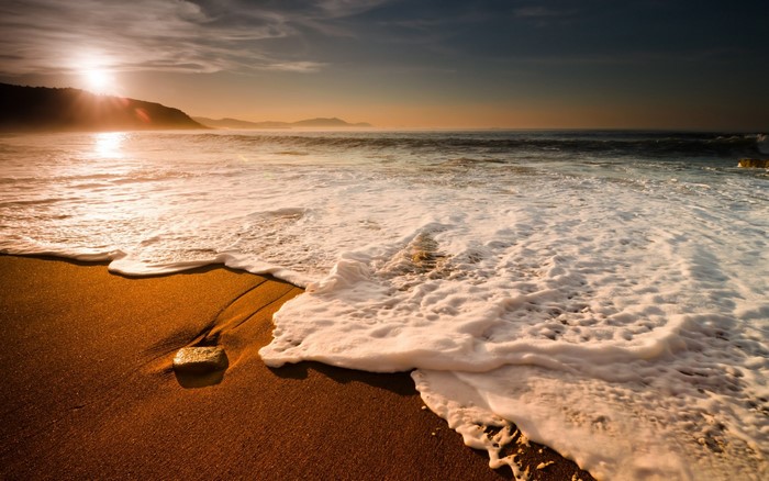 Sunset over the ocean with waves crashing on the shore