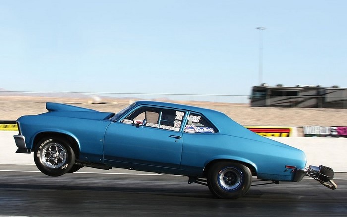 Blue drag racing car performing a wheelie on a track