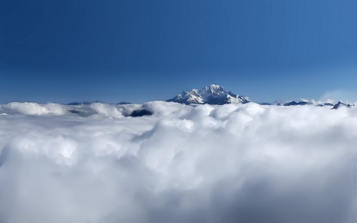 Snow-capped mountains above clouds under a blue sky