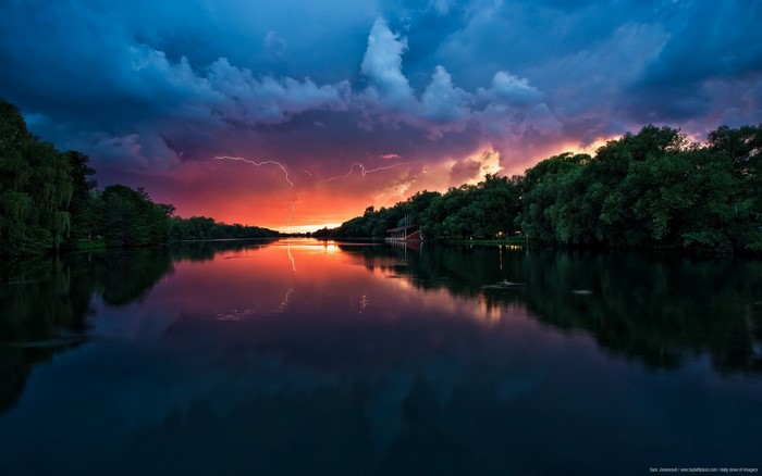 Lightning strikes over a lake at sunset with trees