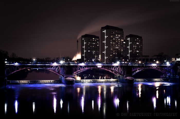 Bridge over river at night with city buildings