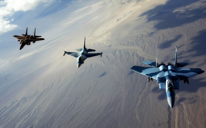 Three fighter jets flying over desert landscape