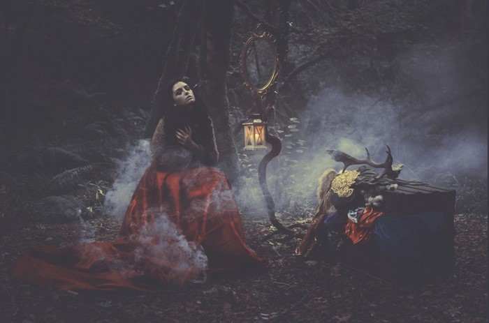 Woman in red dress in foggy forest with mirror and lantern