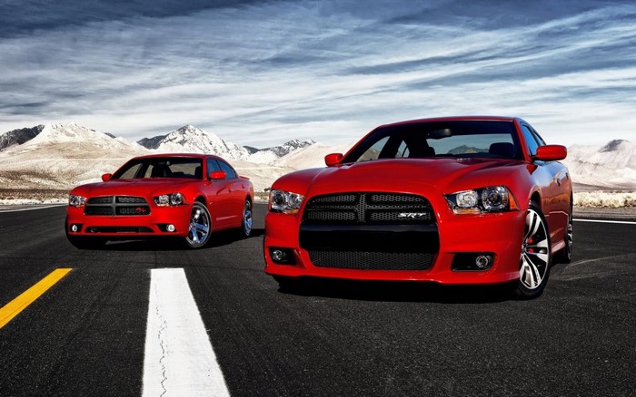 Two red Dodge Chargers on a road with mountains