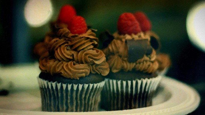 Two chocolate cupcakes with raspberries and chocolate frosting