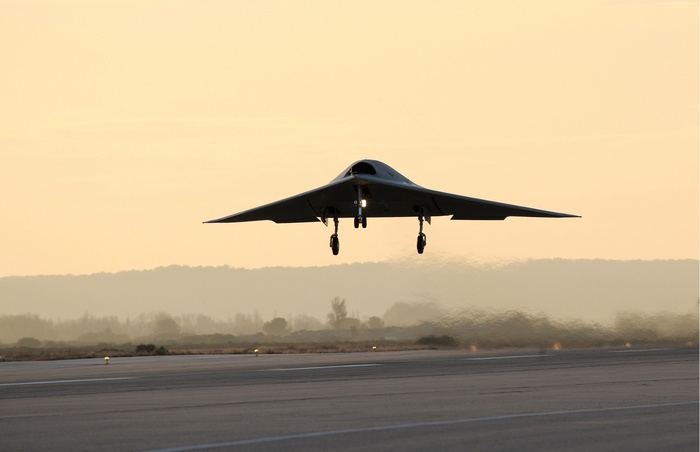 X-47B drone landing on runway at sunset
