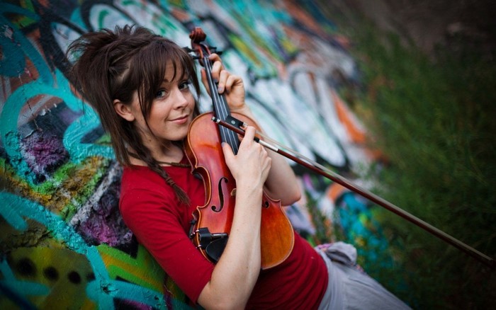 Woman with violin leaning against graffiti wall
