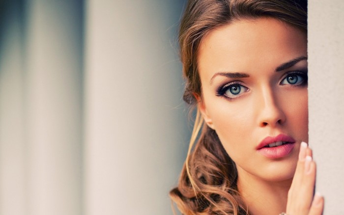Woman with blue eyes and brown hair peeking from behind a wall
