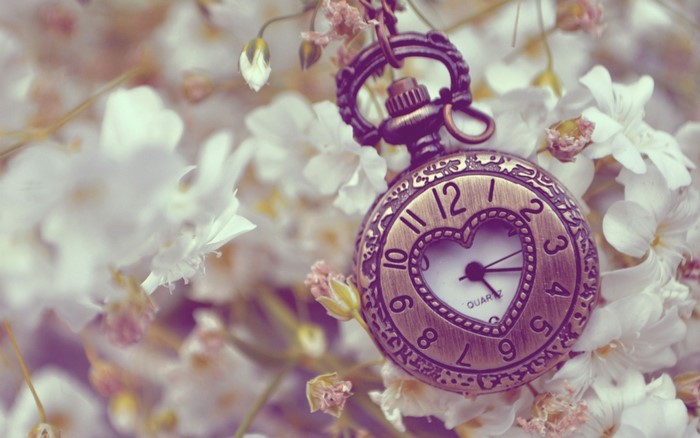 Close-up of a vintage pocket watch with a heart-shaped face surrounded by white flowers