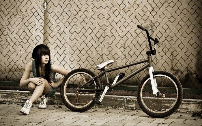 Girl with BMX bike in front of chain-link fence