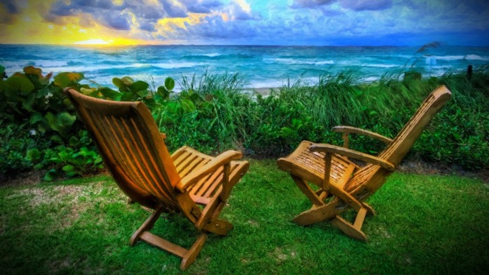 Two wooden chairs on a grassy lawn overlooking the sea