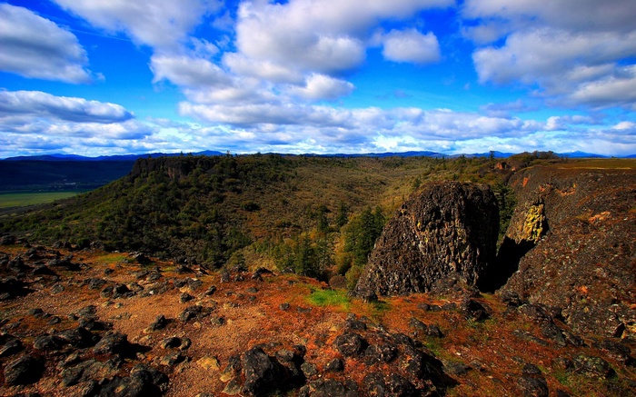 Rocky cliff overlooking a valley under a cloudy sky