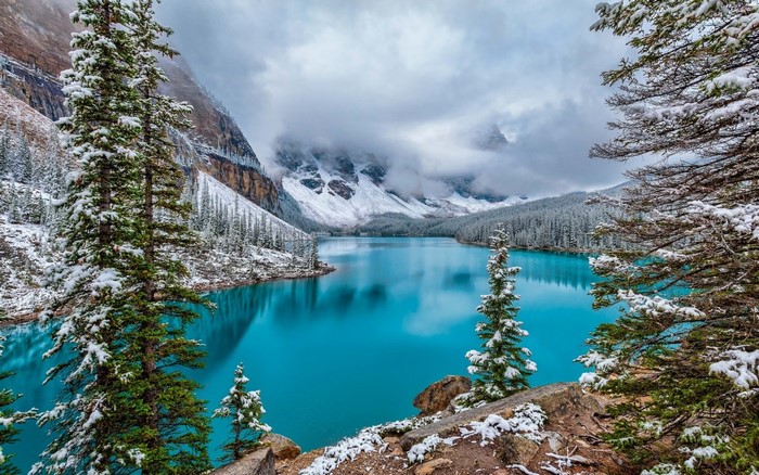 Snow-covered trees and mountains around a bright blue lake
