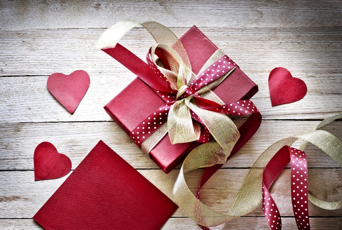 Red gift box with ribbons and hearts on wooden background