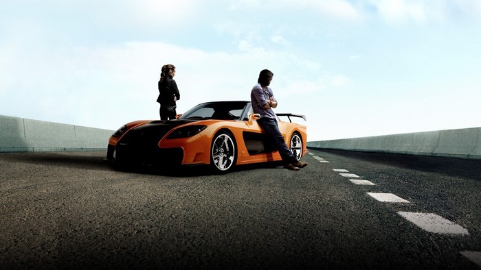 Man and woman with orange sports car on road