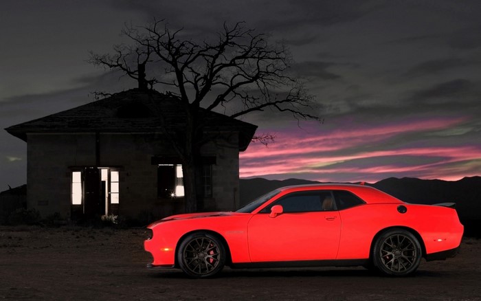 Red Dodge Challenger parked by an abandoned house at dusk