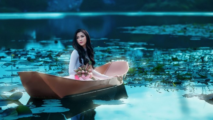 Woman in a boat holding lotus flowers on a lake