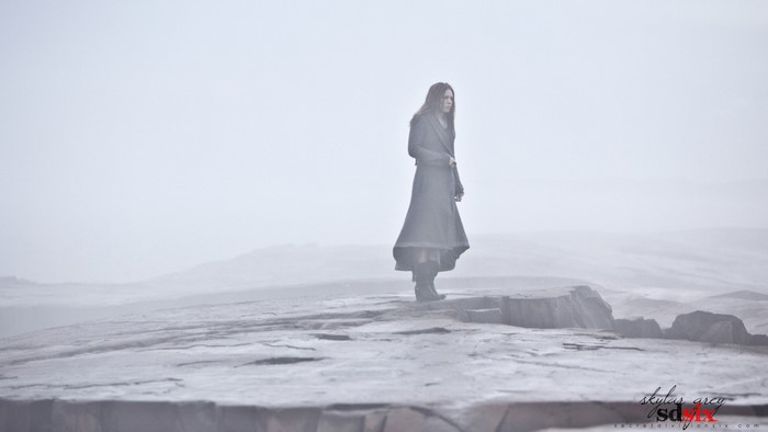 Woman in a long coat standing on a rocky outcrop in fog