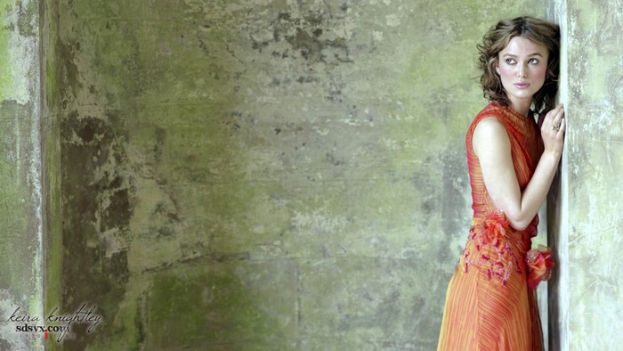 Keira Knightley in an orange dress leaning against a wall