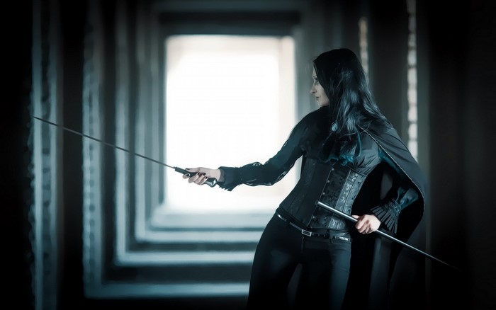 Woman in black holding swords in a dark hallway