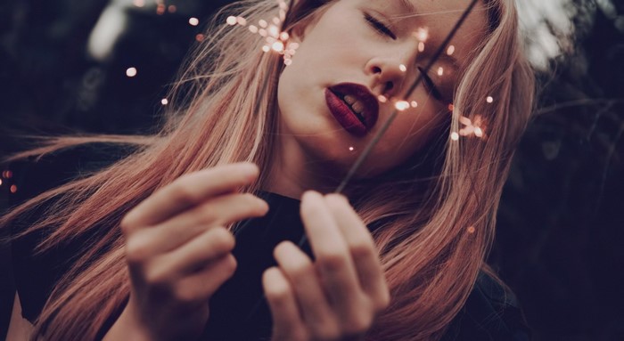 Woman holding sparklers with closed eyes
