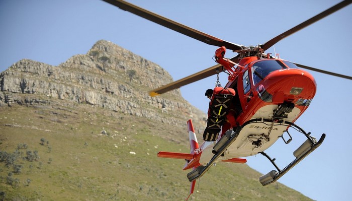 Red helicopter with rescuer in mountainous terrain