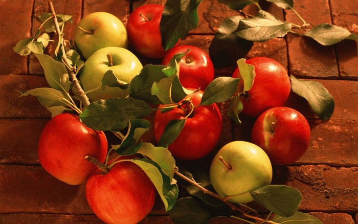 Still life of red and green apples with leaves on brick