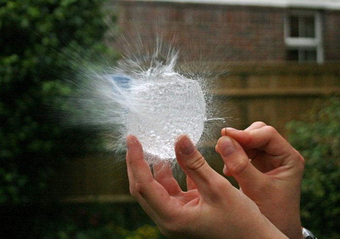 Hands bursting a water balloon with a pin