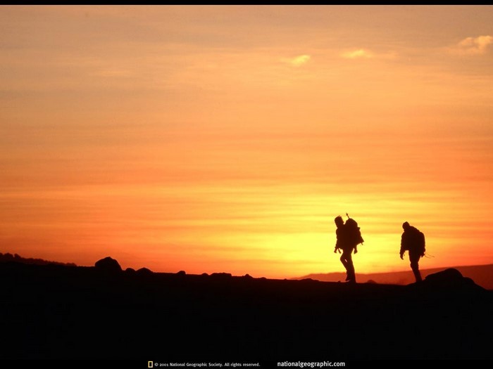 Two hikers silhouetted against a vibrant sunset
