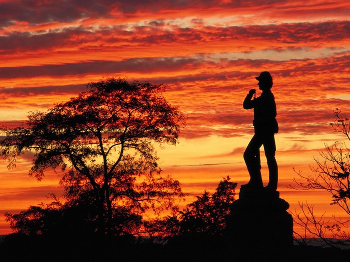 Silhouette of a soldier statue against a sunset sky