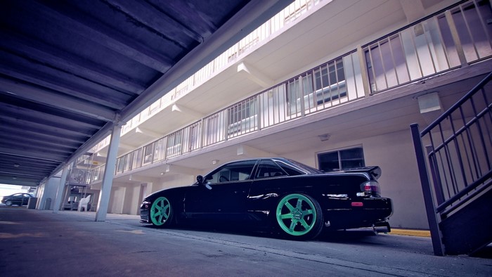Black sports car with green wheels parked under a building