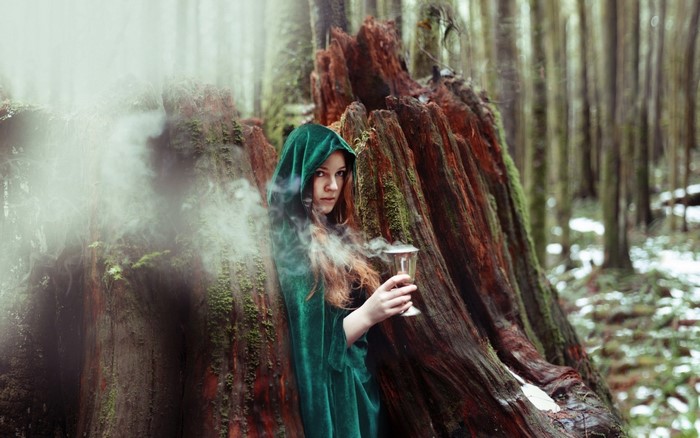 Woman in green cloak holding a chalice in a forest