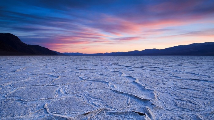 Cracked salt flats at sunset with mountains on the horizon