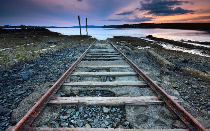 Abandoned railway tracks leading to the sea at sunset