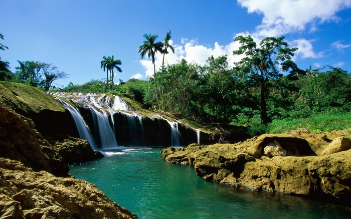 Waterfall cascading over rocks with palm trees and lush greenery