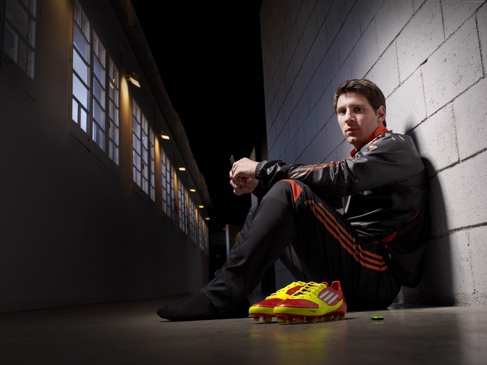Lionel Messi sitting with Adidas soccer cleats