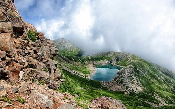 Mountain lake surrounded by green slopes and rocky cliffs under cloudy sky