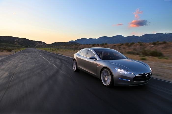 Tesla Model S driving on a road at sunset