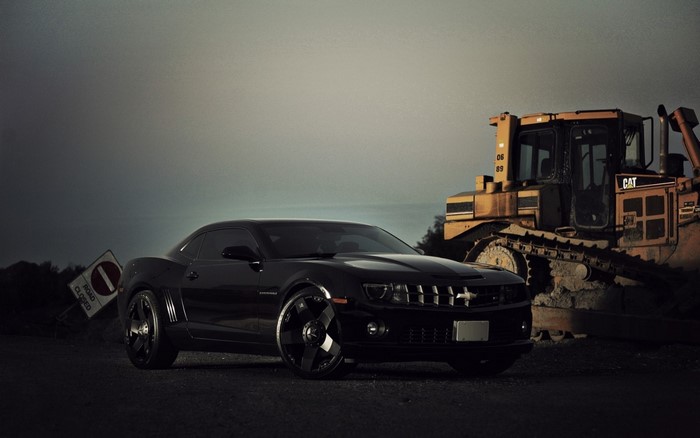 Black Chevrolet Camaro parked near a bulldozer