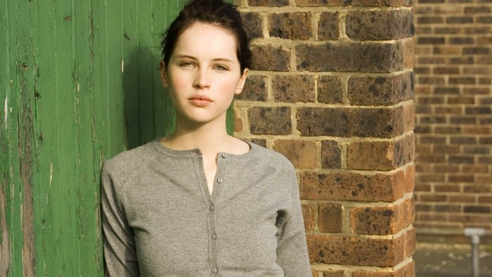 Felicity Jones leaning against a green door and brick wall