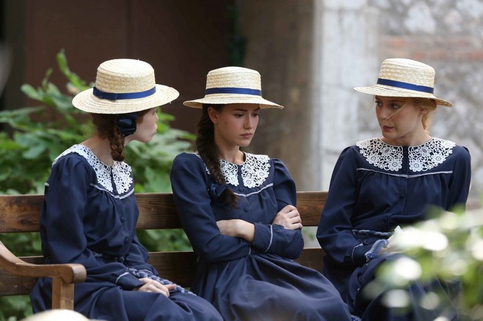 Three women in school uniforms and hats sitting on a bench