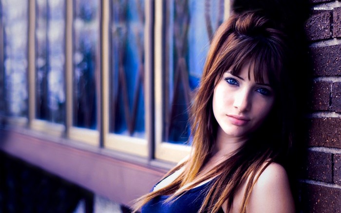 Woman with blue eyes leaning against a brick wall